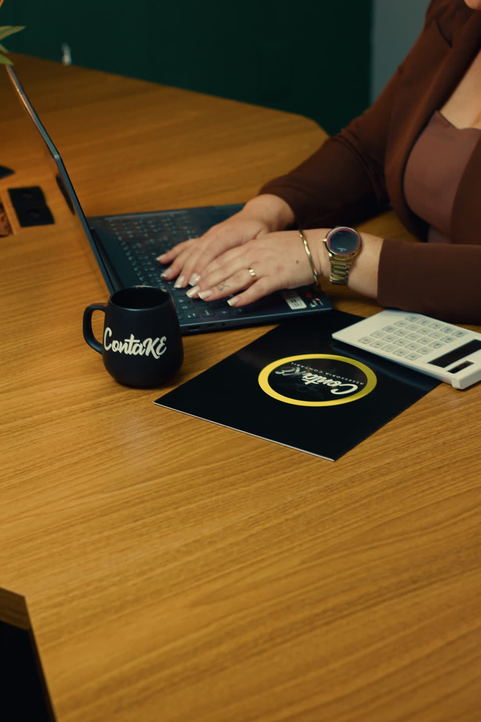 Ketlyn trabalhando no notebook, com a caneca da ContaKE sobre a mesa